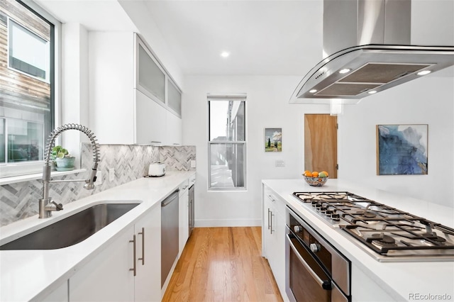 kitchen featuring sink, appliances with stainless steel finishes, white cabinetry, island range hood, and decorative backsplash