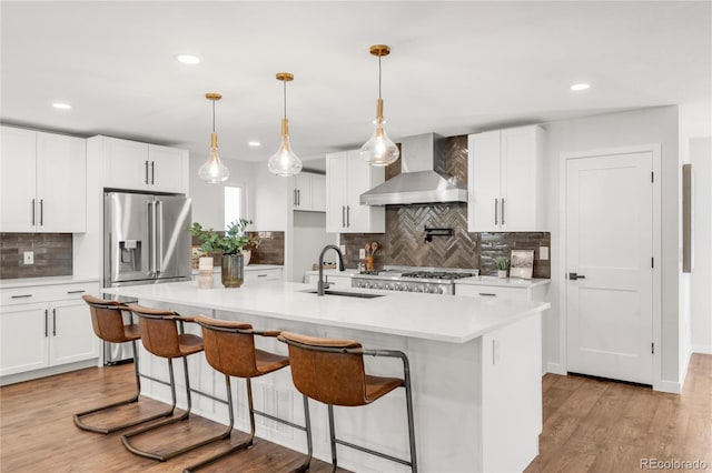 kitchen featuring a center island with sink, white cabinetry, and wall chimney range hood