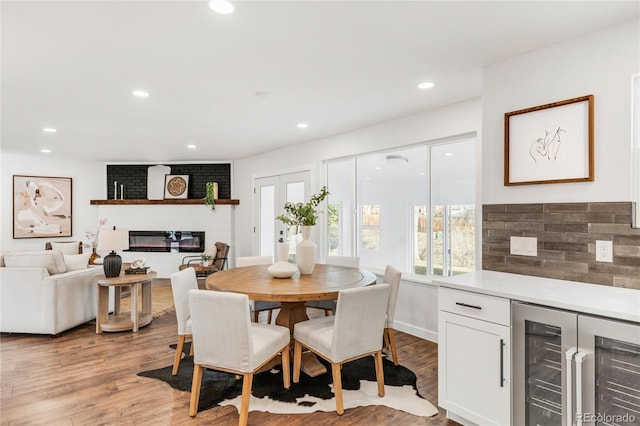 dining space featuring bar area, wine cooler, light wood-type flooring, and a brick fireplace