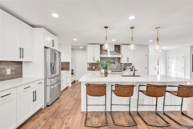 kitchen with high quality fridge, a kitchen island with sink, white cabinets, and wall chimney range hood