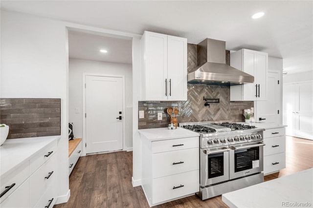 kitchen with tasteful backsplash, wall chimney exhaust hood, dark wood-type flooring, range with two ovens, and white cabinets