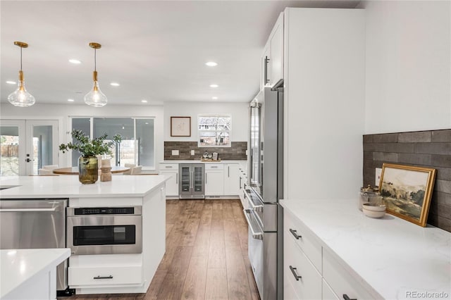 kitchen featuring tasteful backsplash, light stone counters, stainless steel appliances, decorative light fixtures, and white cabinets