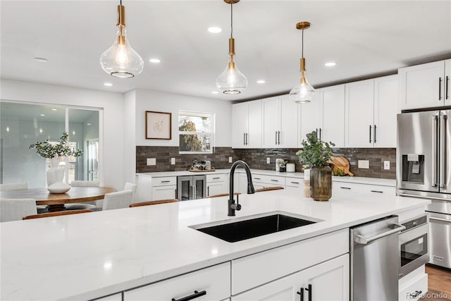 kitchen with light stone countertops, white cabinetry, sink, hanging light fixtures, and appliances with stainless steel finishes