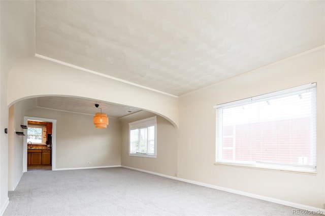 empty room with arched walkways, light carpet, and baseboards