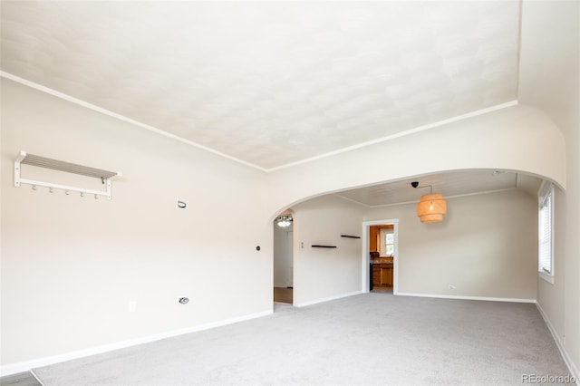 unfurnished room featuring arched walkways, light colored carpet, plenty of natural light, and baseboards