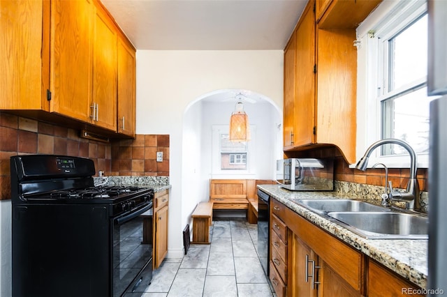 kitchen featuring arched walkways, brown cabinets, decorative backsplash, a sink, and black appliances