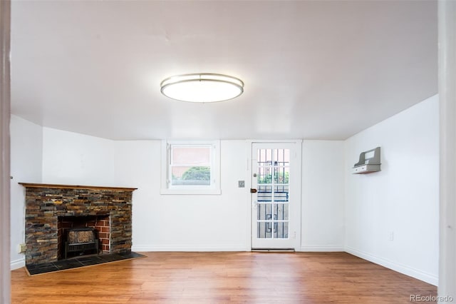 unfurnished living room featuring a fireplace with flush hearth, wood finished floors, and baseboards