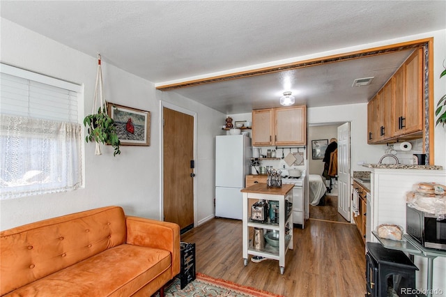 kitchen with gas range oven, visible vents, freestanding refrigerator, a textured ceiling, and wood finished floors