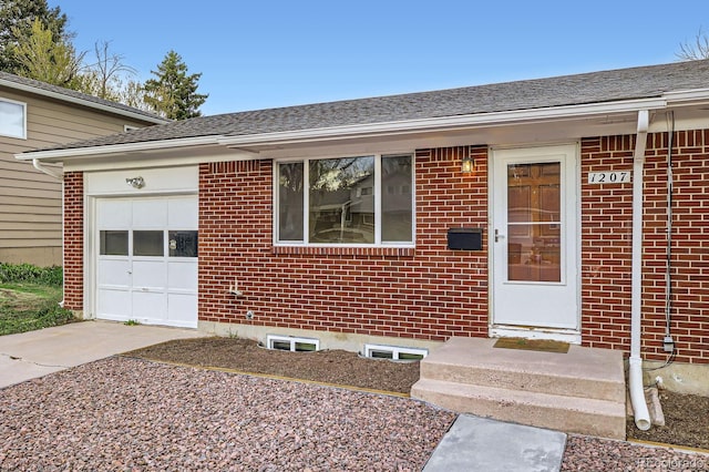 1207 Kingsley Dr, Colorado Springs, CO 80909 - view of exterior entry with an attached garage, brick siding, driveway, and a shingled roof