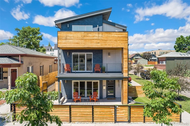 back of property featuring a fenced front yard, brick siding, a patio, and a balcony