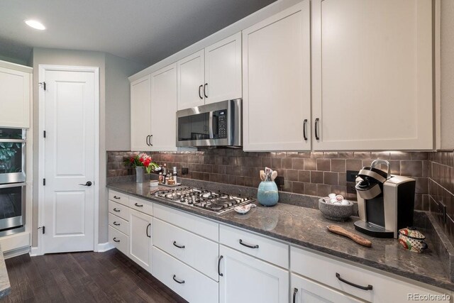 565 Pikes View Dr, Erie, CO 80516 - kitchen with stainless steel appliances, dark stone countertops, white cabinetry, dark wood-style flooring, and tasteful backsplash
