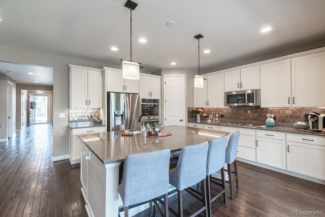 565 Pikes View Dr, Erie, CO 80516 - kitchen featuring appliances with stainless steel finishes, dark wood-type flooring, decorative backsplash, a center island with sink, and recessed lighting