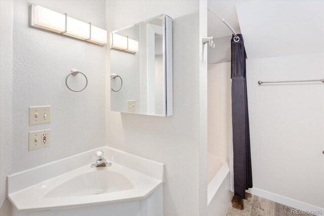 bathroom featuring a sink, shower / bath combination with curtain, wood finished floors, and baseboards