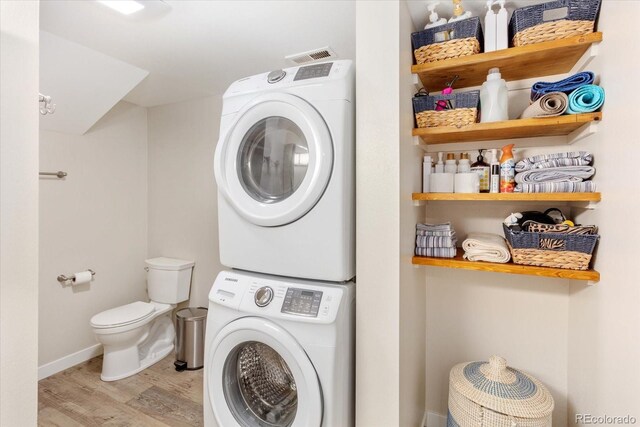 laundry room with laundry area, stacked washing maching and dryer, light wood-style flooring, and baseboards