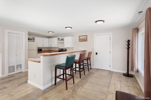 kitchen featuring a peninsula, white cabinets, light countertops, open shelves, and light wood finished floors