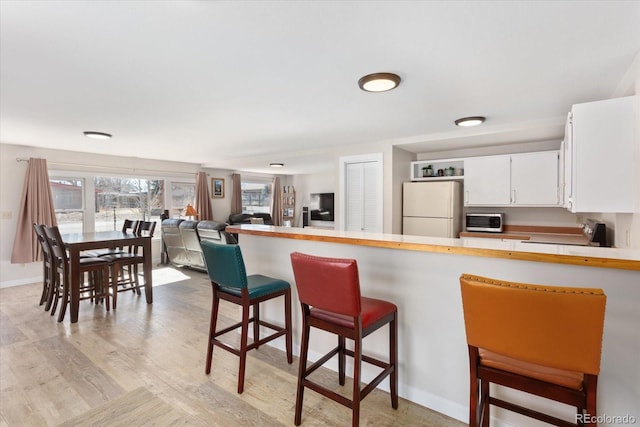 kitchen featuring light countertops, freestanding refrigerator, white cabinetry, range, and a kitchen bar