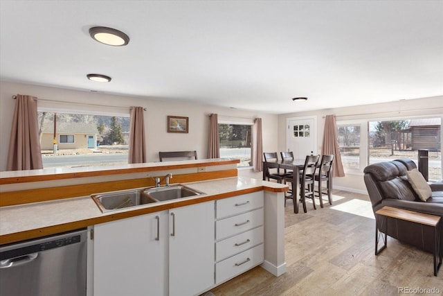 kitchen with light countertops, stainless steel dishwasher, a sink, and white cabinetry