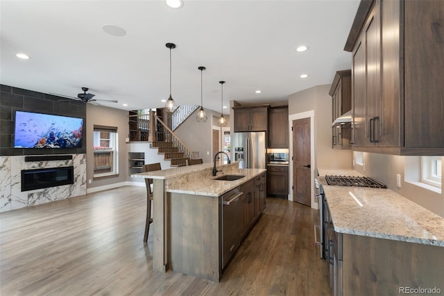 kitchen featuring sink, a breakfast bar, a fireplace, an island with sink, and decorative light fixtures