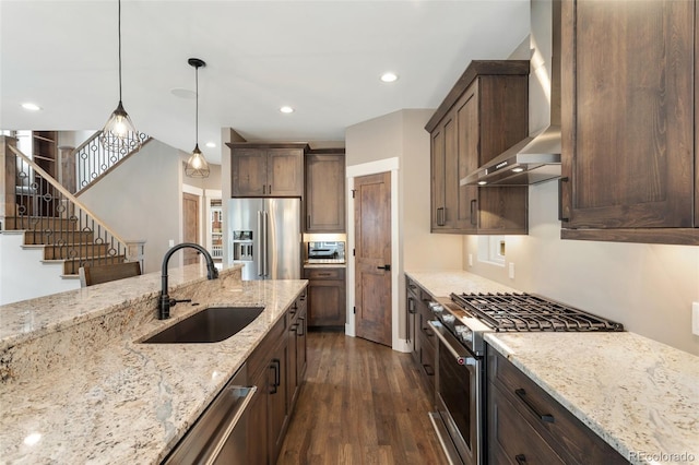 kitchen featuring sink, light stone counters, appliances with stainless steel finishes, pendant lighting, and wall chimney range hood