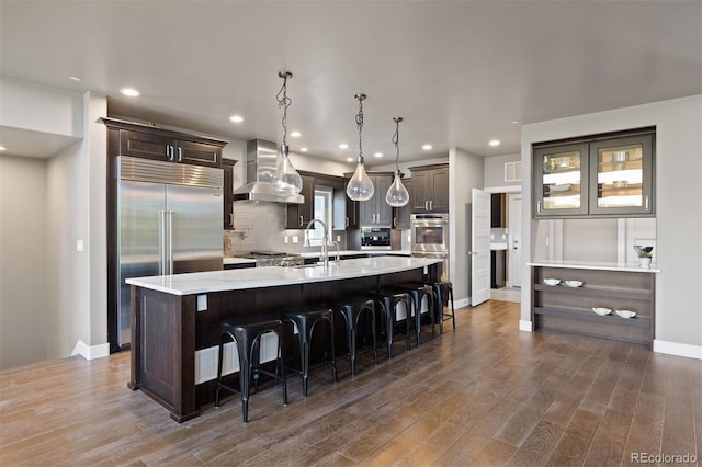 1803 Avenida Del Sol, Castle Rock, CO 80104 - kitchen with wall chimney range hood, stainless steel appliances, light countertops, dark brown cabinets, and a large island with sink