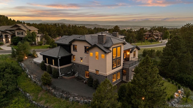 1803 Avenida Del Sol, Castle Rock, CO 80104 - back of property at dusk featuring a balcony, stone siding, a chimney, driveway, and a garage