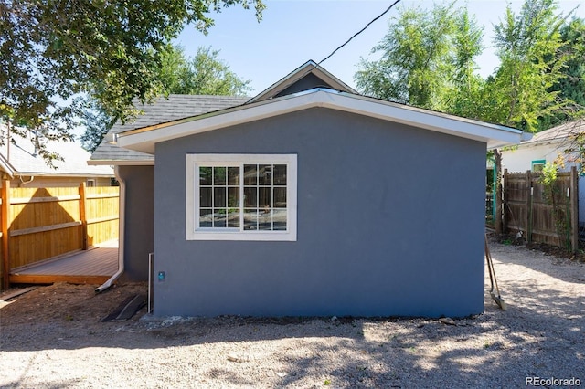 exterior space with stucco siding, roof with shingles, and fence