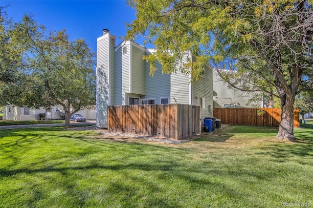 view of side of property with a yard, fence, and a chimney