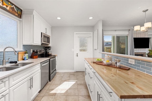 kitchen featuring wooden counters, a sink, decorative backsplash, white cabinets, and appliances with stainless steel finishes