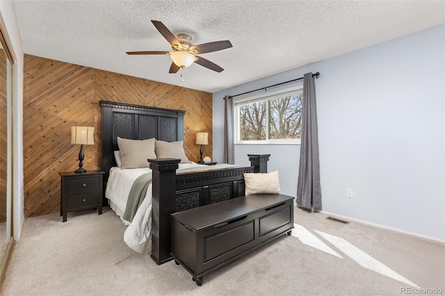 bedroom featuring visible vents, light carpet, wooden walls, and a textured ceiling