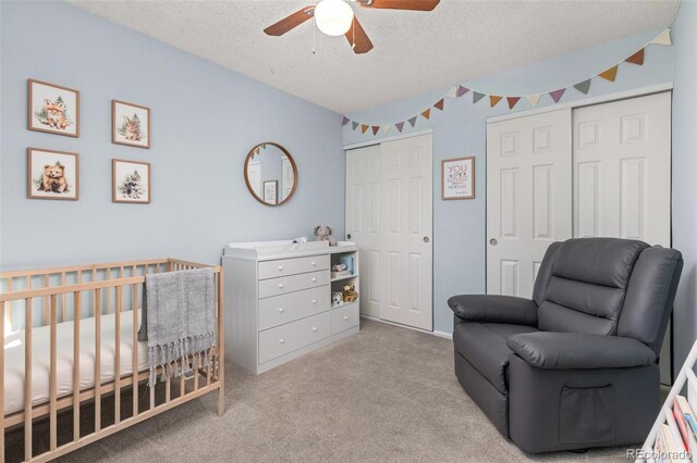 bedroom featuring ceiling fan, a crib, a textured ceiling, carpet flooring, and two closets