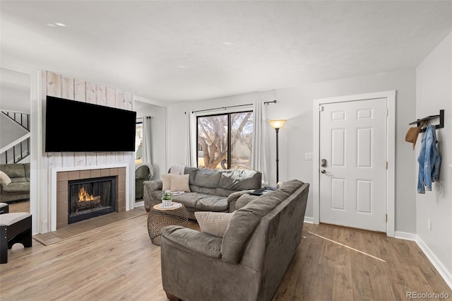 living area with a tiled fireplace, baseboards, and wood finished floors