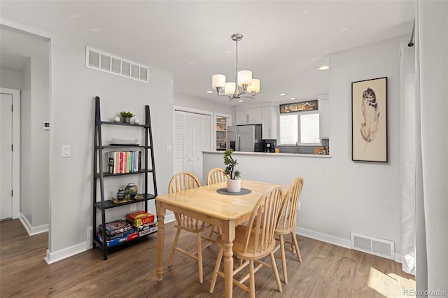 dining area with a notable chandelier, visible vents, baseboards, and wood finished floors