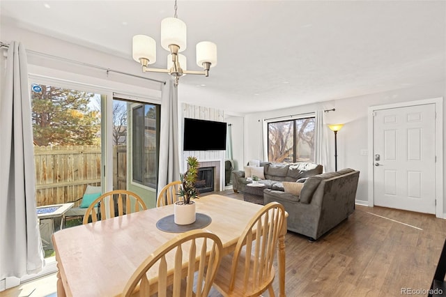 dining room with light wood-style flooring, a notable chandelier, a fireplace, and baseboards