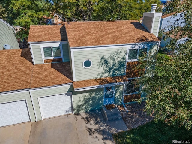 view of front of home with a garage, concrete driveway, a chimney, and roof with shingles