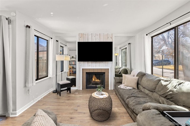 living area with light wood-type flooring, baseboards, and a tiled fireplace