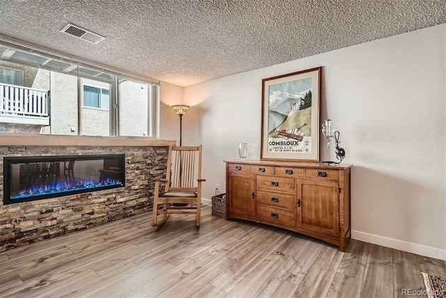 living area featuring a stone fireplace, a textured ceiling, and light hardwood / wood-style flooring