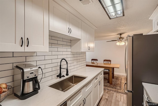 kitchen with sink, stainless steel refrigerator, light stone countertops, white cabinetry, and light hardwood / wood-style flooring