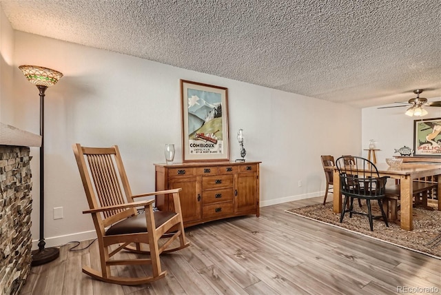 living area with light hardwood / wood-style floors, ceiling fan, and a textured ceiling