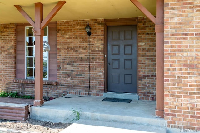 doorway to property featuring a porch and brick siding