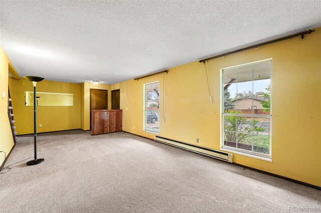 carpeted spare room featuring a baseboard heating unit, a textured ceiling, and baseboards