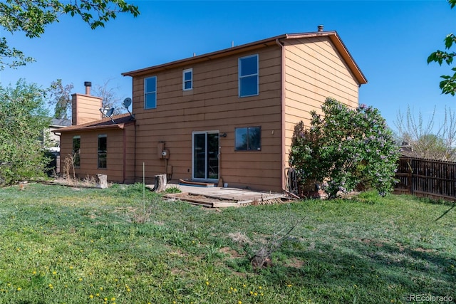 rear view of property with a chimney, a patio area, a yard, and fence