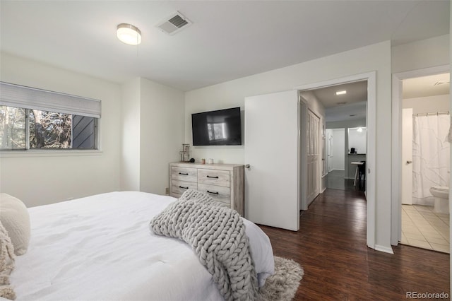 bedroom with visible vents, dark wood-type flooring, and connected bathroom