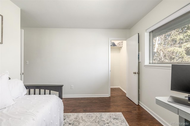 bedroom featuring a walk in closet, baseboards, and wood finished floors