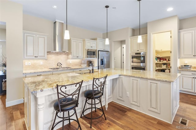 kitchen featuring light wood-style flooring, a sink, visible vents, wall chimney range hood, and appliances with stainless steel finishes