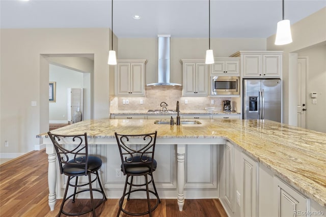 kitchen featuring light stone counters, stainless steel appliances, a sink, wall chimney exhaust hood, and tasteful backsplash