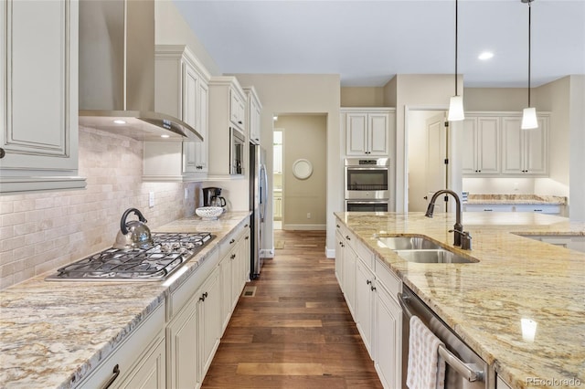 kitchen featuring a sink, wall chimney range hood, appliances with stainless steel finishes, dark wood-style floors, and decorative light fixtures