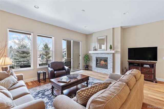 living area featuring light wood-type flooring, a stone fireplace, baseboards, and recessed lighting