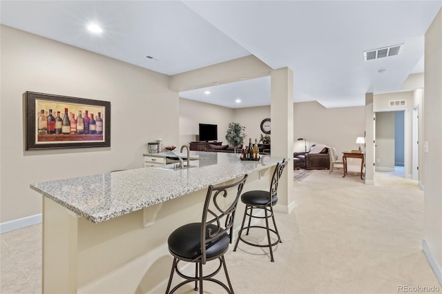 kitchen featuring light stone counters, a kitchen bar, a sink, and visible vents