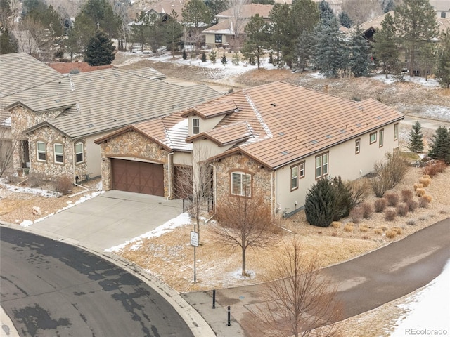 view of front of property with stucco siding, a garage, stone siding, driveway, and a tiled roof