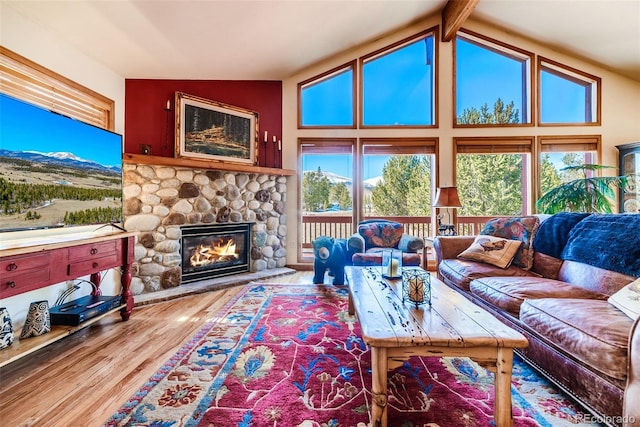 living area featuring a stone fireplace, vaulted ceiling with beams, and wood finished floors